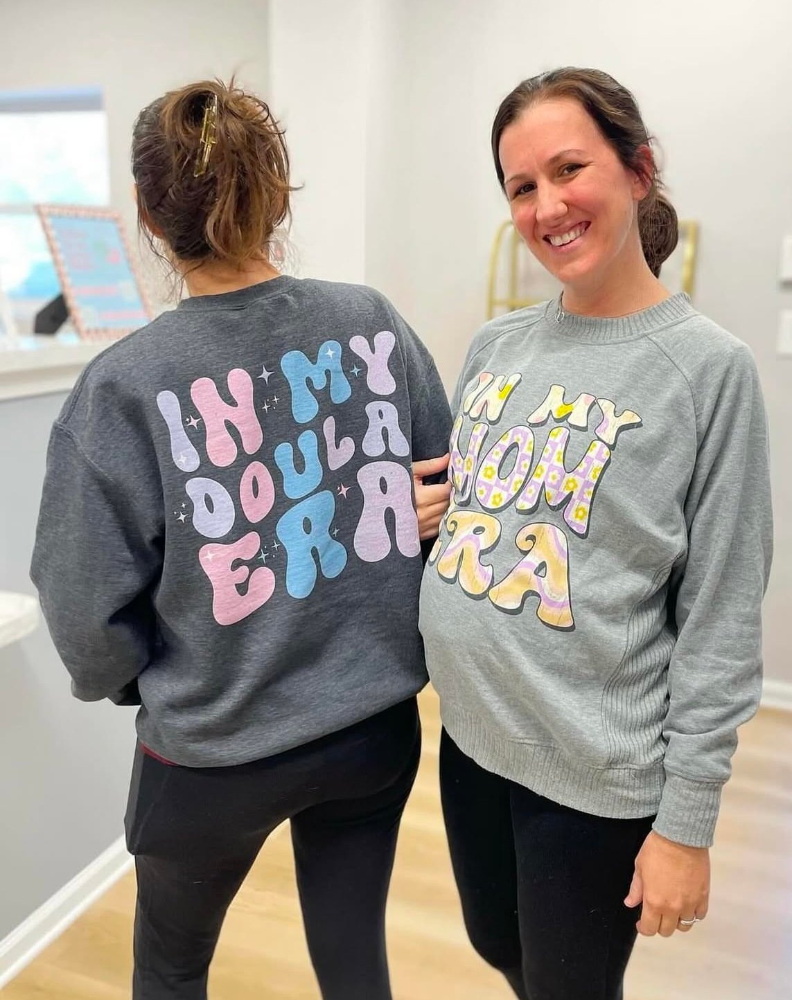 A doula and an expectant mother wearing themed sweatshirts, celebrating their childbirth journey.