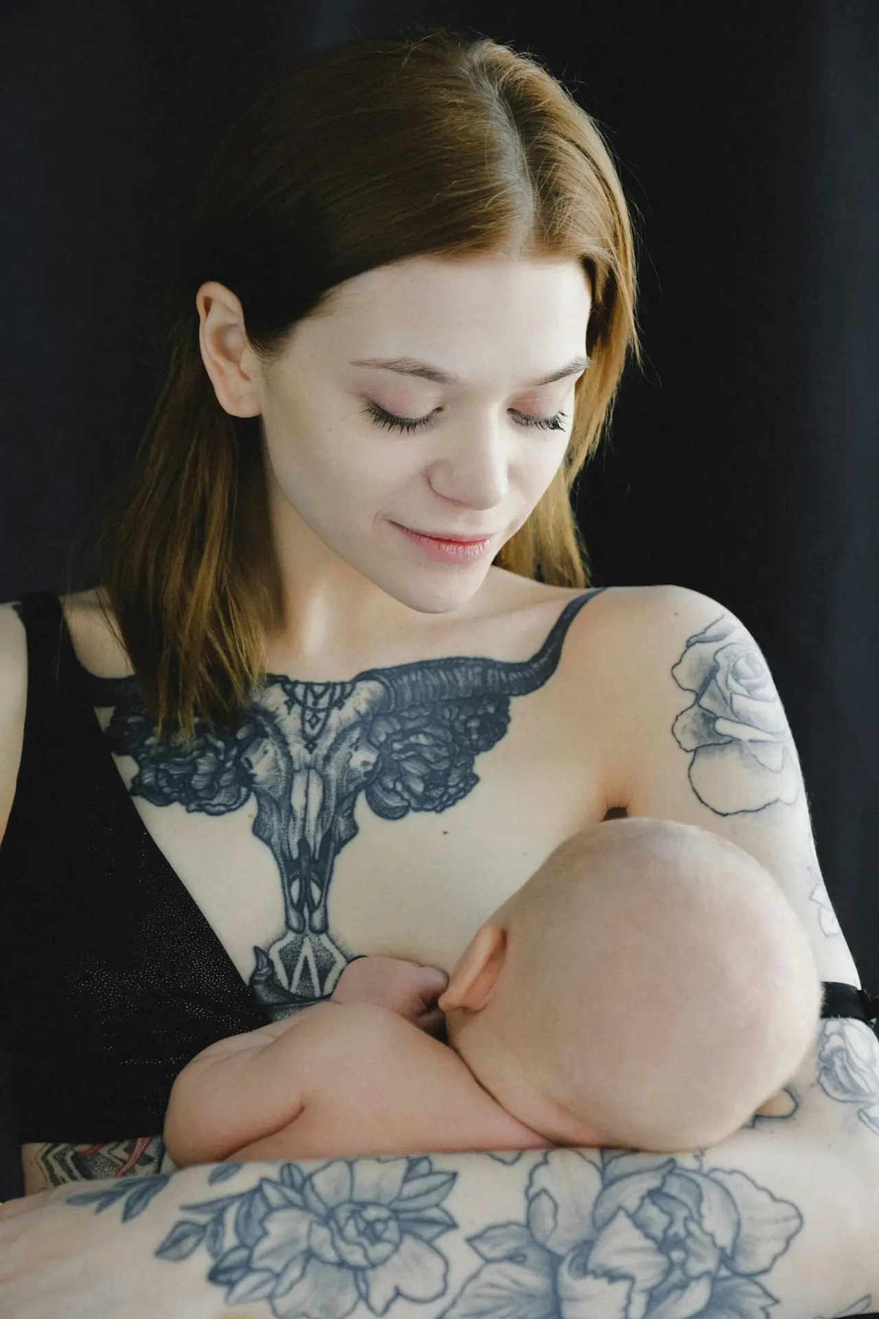 A tattooed mother lovingly breastfeeds her baby, showcasing the bond of motherhood.